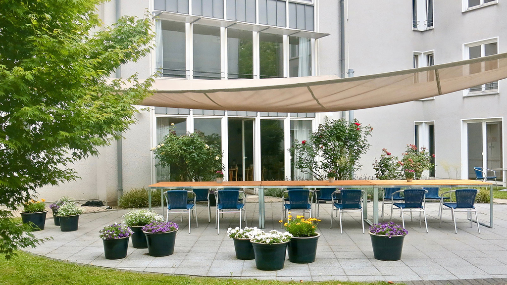 Innenhof des Convenio Gelsenkirchen mit Sonnensegel, langer Tafel und Blumenkübeln