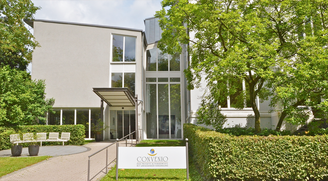 Eingang des Convenio Gelsenkirchen mit Vordach und Namensschild zwischen Hecken und Bäumen
