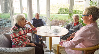 Bewohner im Gespräch mit einer Mitarbeiterin im Wintergarten des Convenio Gelsenkirchen